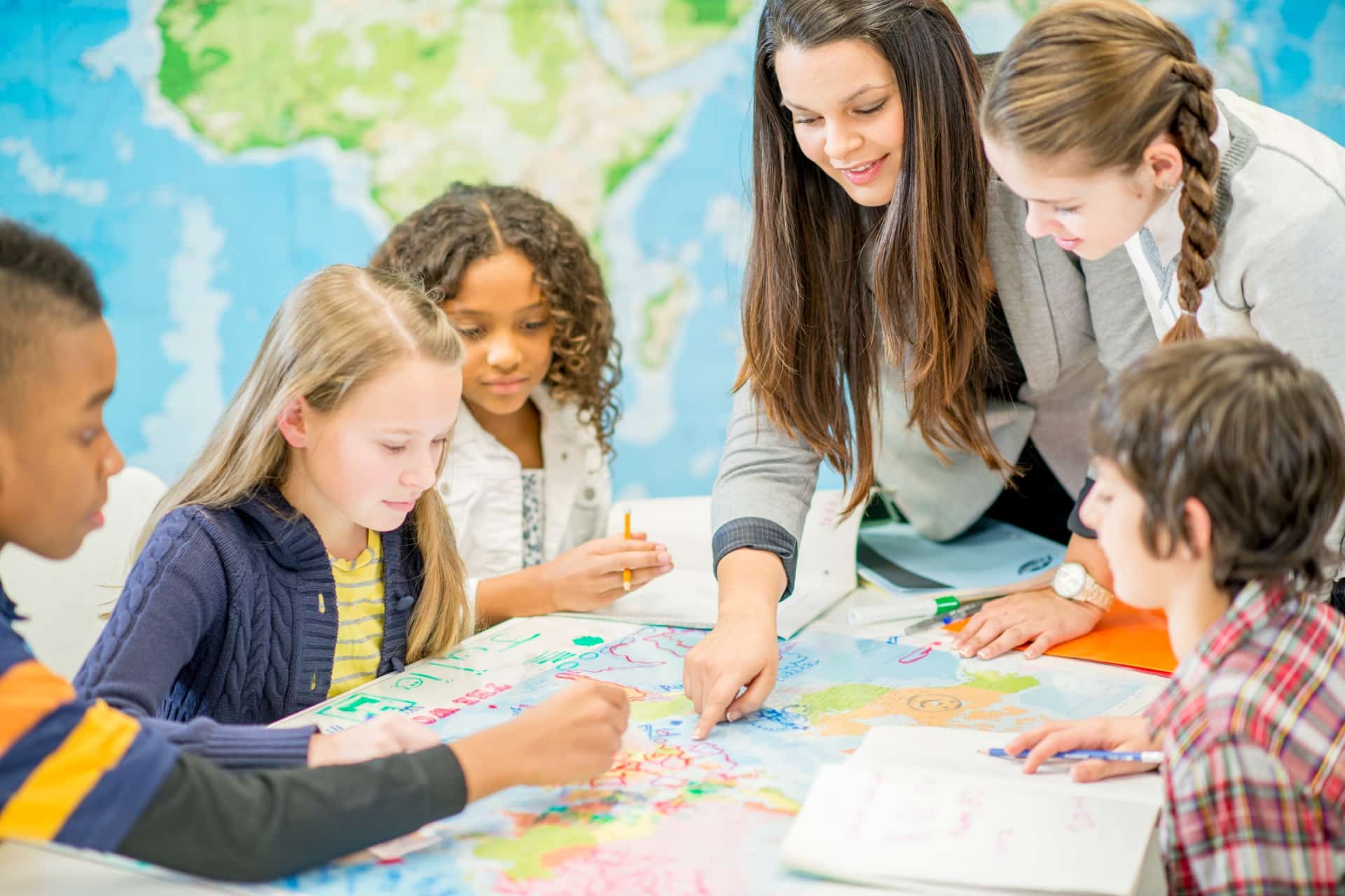 This is a photo of some young students and their teacher examining a large map.